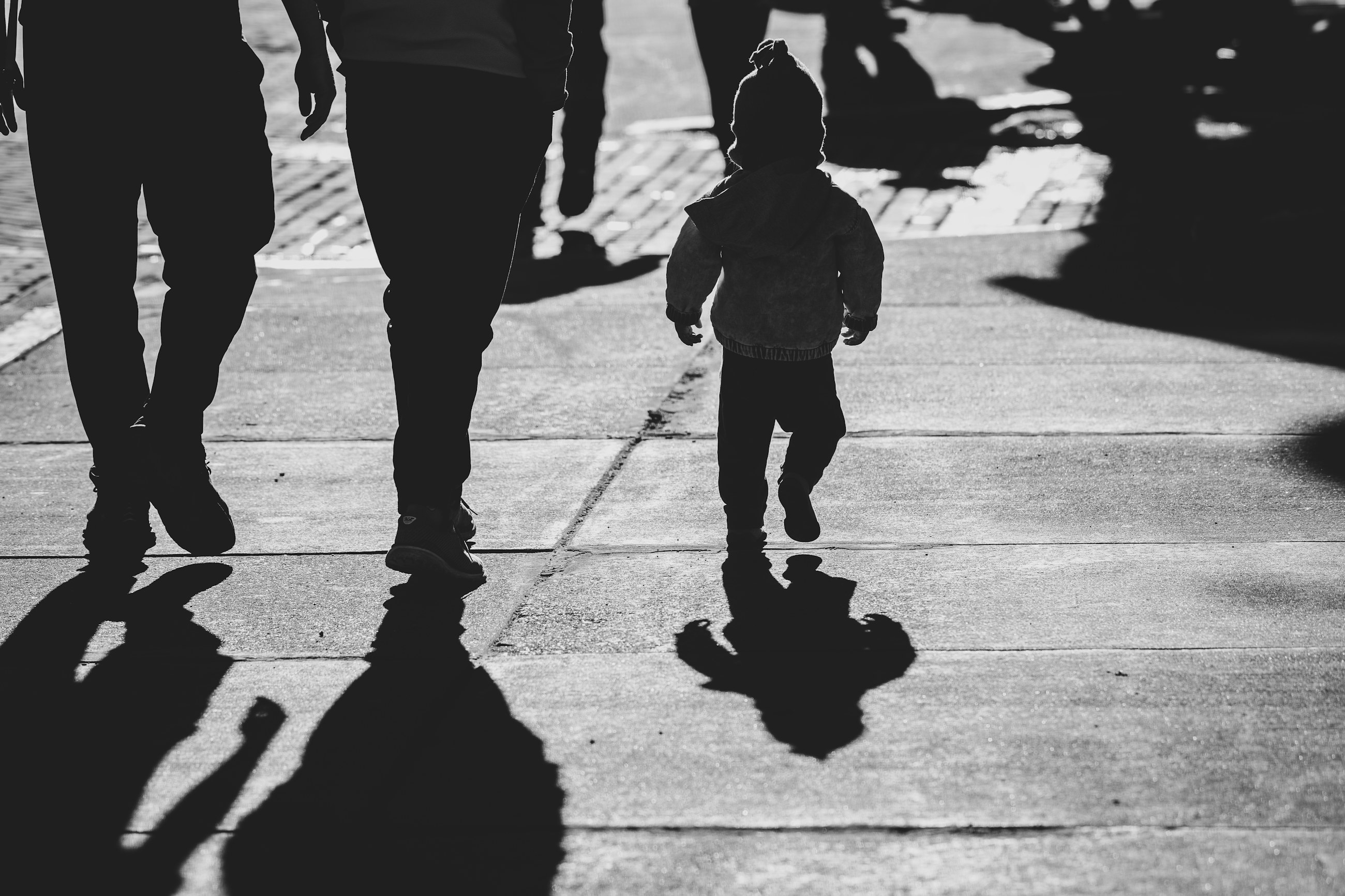 Niño pequeño caminando de espaldas junto a dos adultos